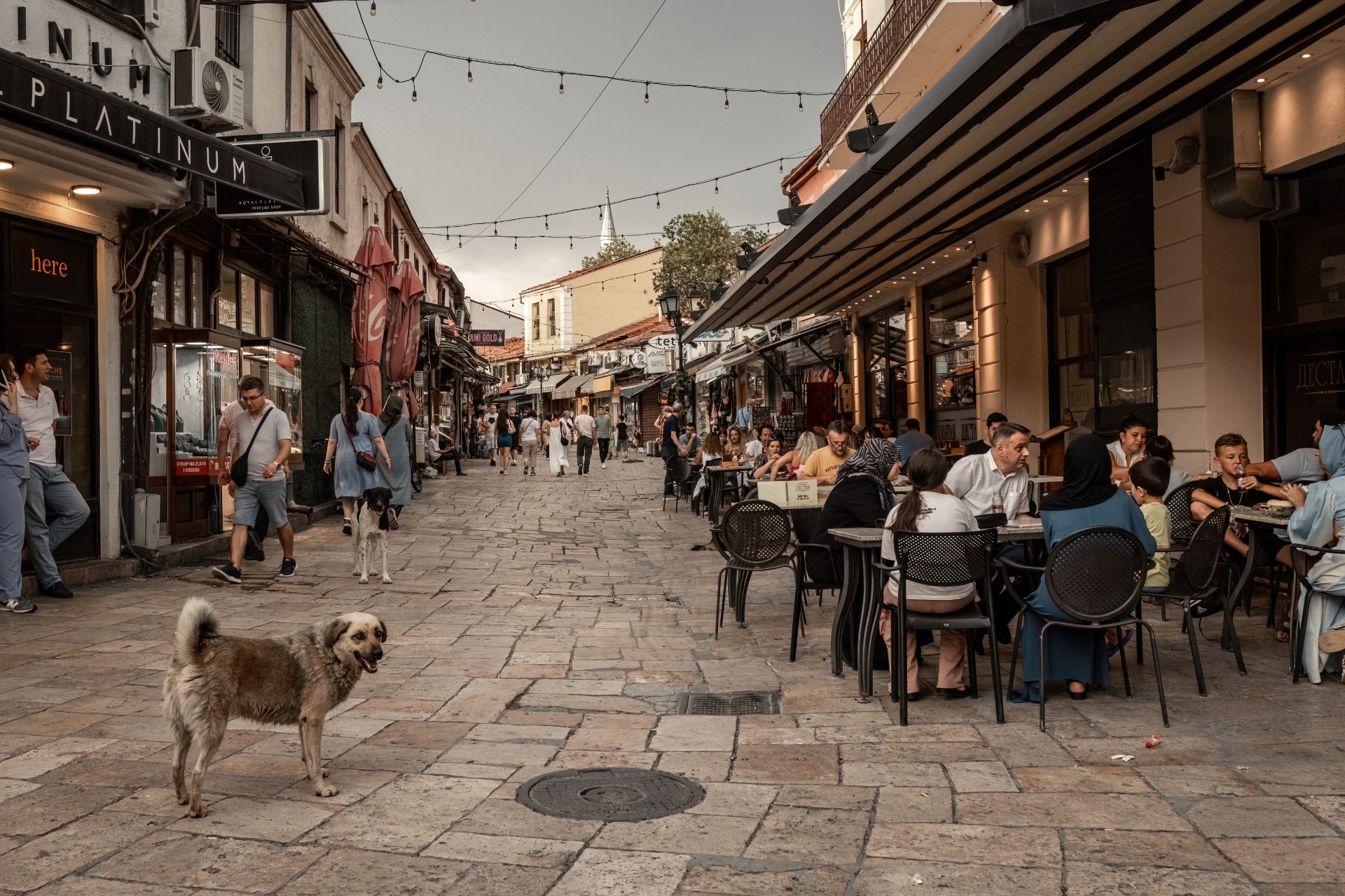 Persone ai tavolini dei caffè in una stretta via del mercato nel centro storico di Skopje